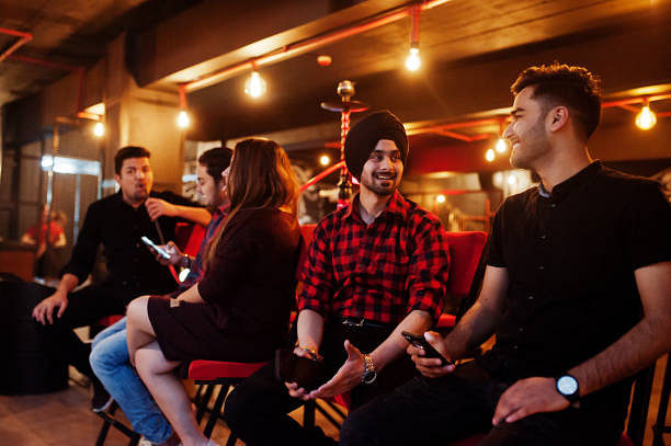 Group of indian friends sitting at lounge bar, smoke hookah and having rest.